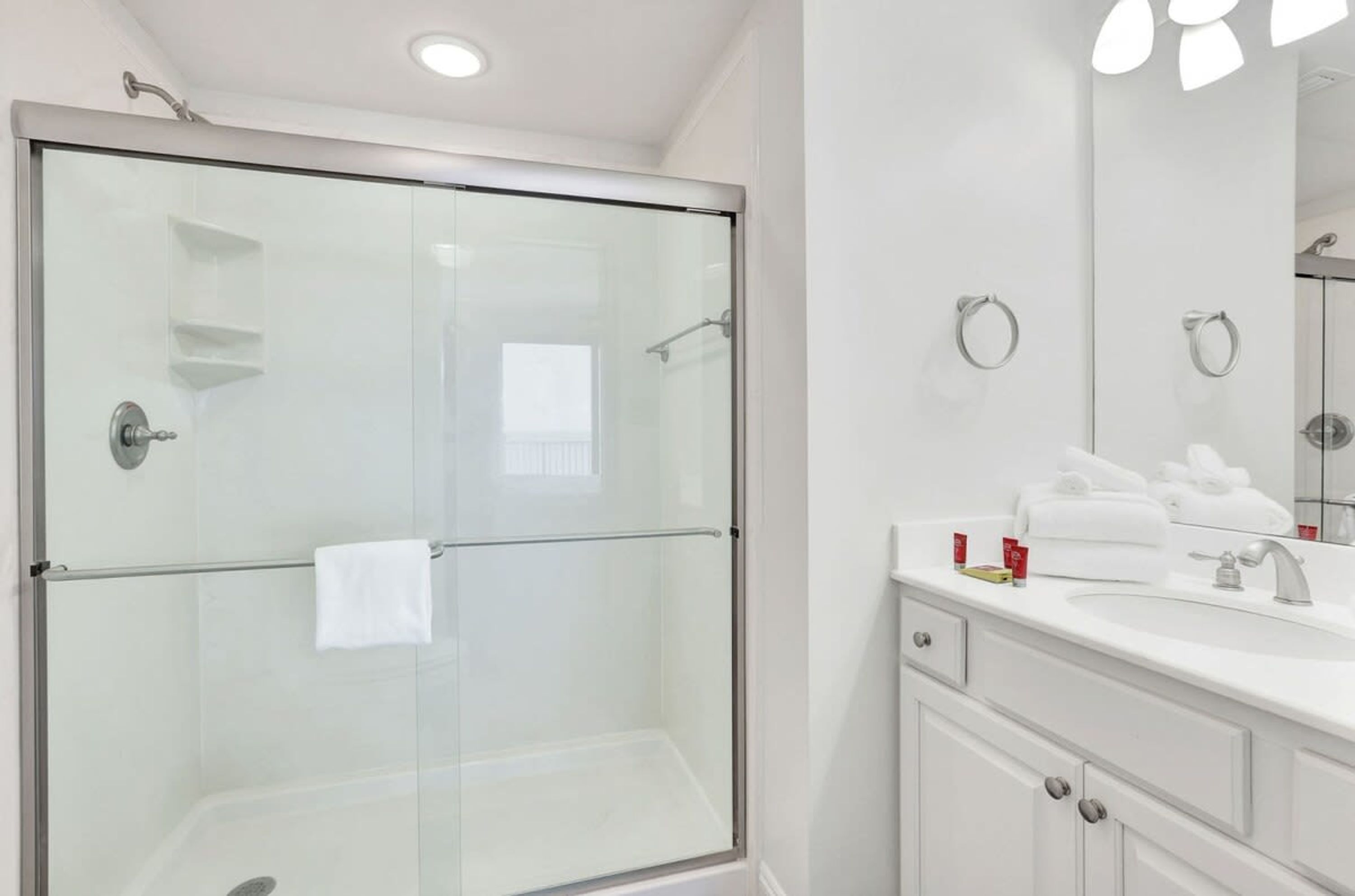 A modern bathroom with a glass-enclosed shower, a white vanity with a sink, and a large mirror.