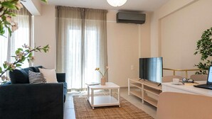 A modern living room with a dark sofa, a white coffee table, a TV, and a laptop on a desk. - Home Easy Kalamata Central Getaway Priv Parking (Kalamata)