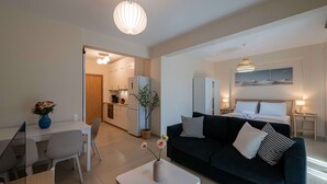 A modern living room with a sofa, a dining table, and a kitchen in the background. - Home Easy Kalamata Central Getaway Priv Parking (Kalamata)