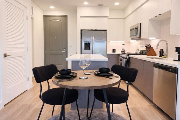 A modern kitchen with a central island, stainless steel appliances, and a dining area with two chairs and a table set for two. - Stylish Stay 10 Min to Disneyland Pool GYM (Santa Ana)