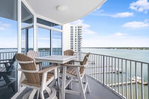 Een balkon met een tafel en stoelen, met uitzicht op een wateroppervlak en een gebouw in de verte.