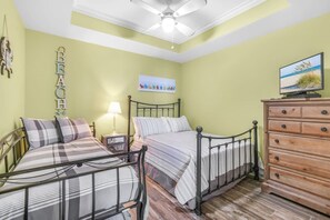 A bedroom with two beds, a dresser, a ceiling fan, a lamp, and a painting on the wall. - Bel Sole 1102  Spacious  water view  beach access (Gulf Shores)