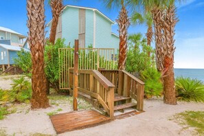 A wooden staircase leading to a light blue building surrounded by palm trees and a sandy beach. - Bel Sole 1102  Spacious  water view  beach access (Gulf Shores)