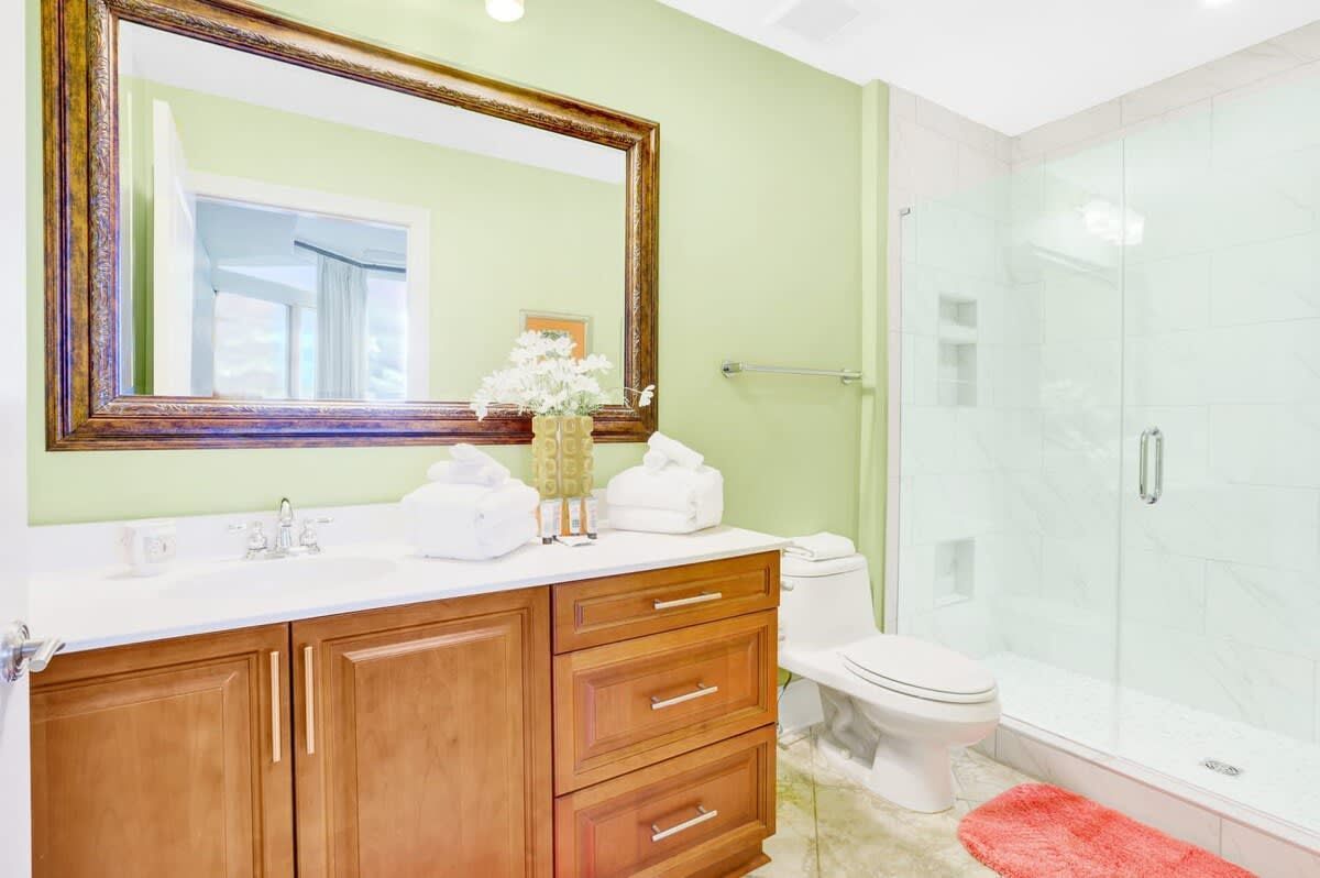 Une salle de bain avec un meuble-lavabo en bois, des toilettes blanches, une cabine de douche en verre et un miroir avec un cadre en bois.