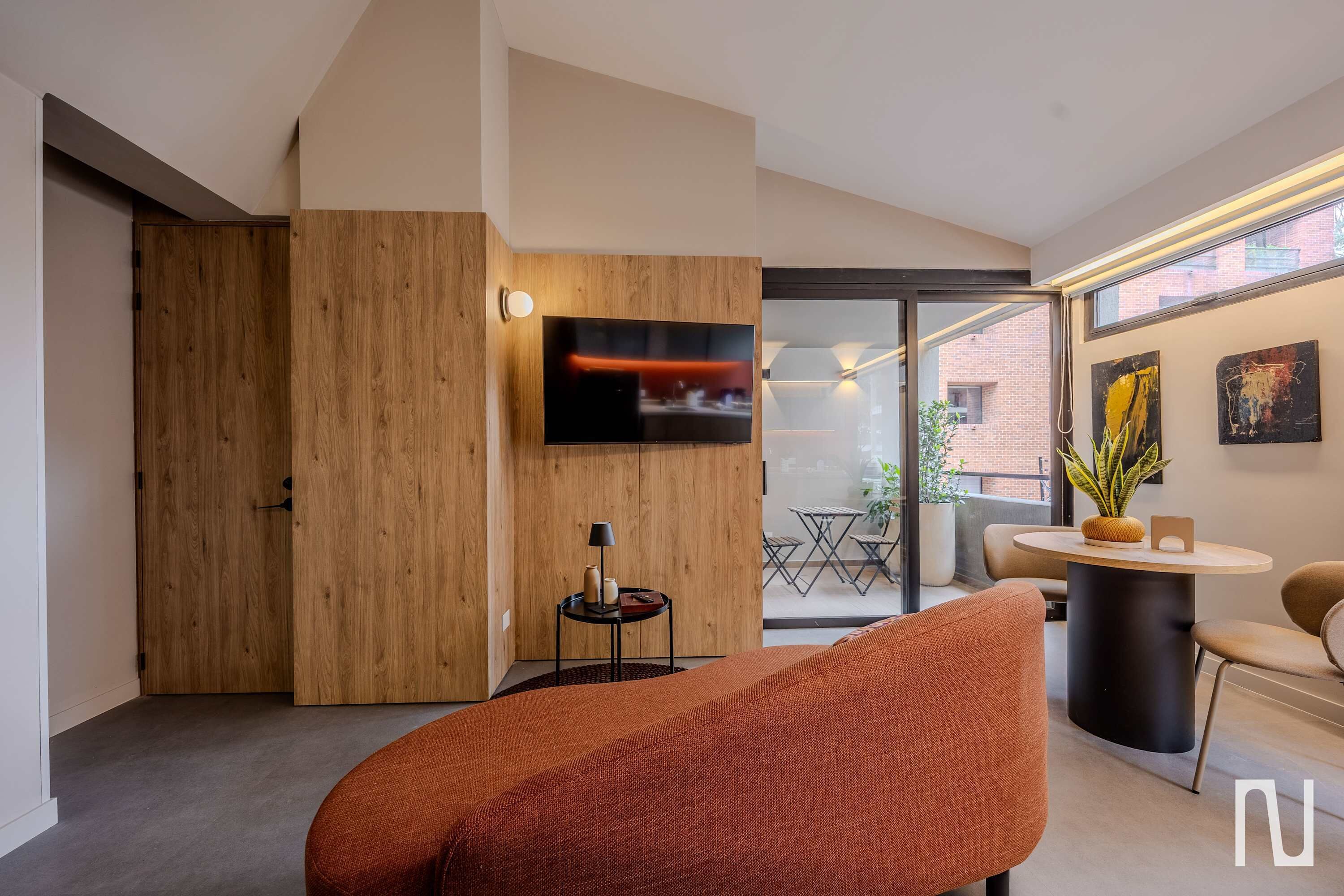 A modern living room with a flat-screen TV, a wooden door, a round table with chairs, and a potted plant.