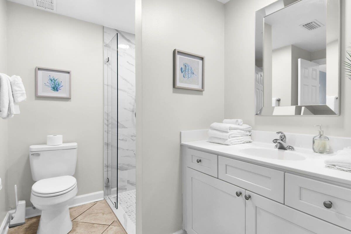 A bathroom with a toilet, a shower, a sink, and a mirror.