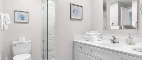 A bathroom with a toilet, a shower, a sink, and a mirror.