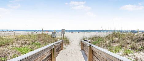 A wooden boardwalk leading to a sandy beach with a clear sky.