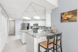 Een moderne keuken met witte kasten, een centraal eiland met barkrukken, en een magnetron.