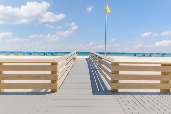 A wooden boardwalk leading to a beach with a flag. - Island Royale- Beachfront Penthouse (Gulf Shores)