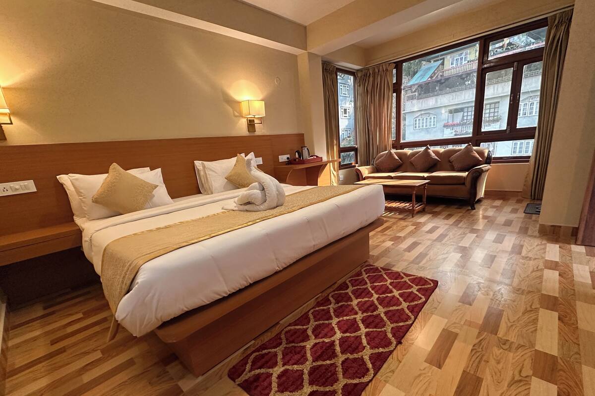 A hotel room with a large bed, a sofa, a TV, and a window with curtains.