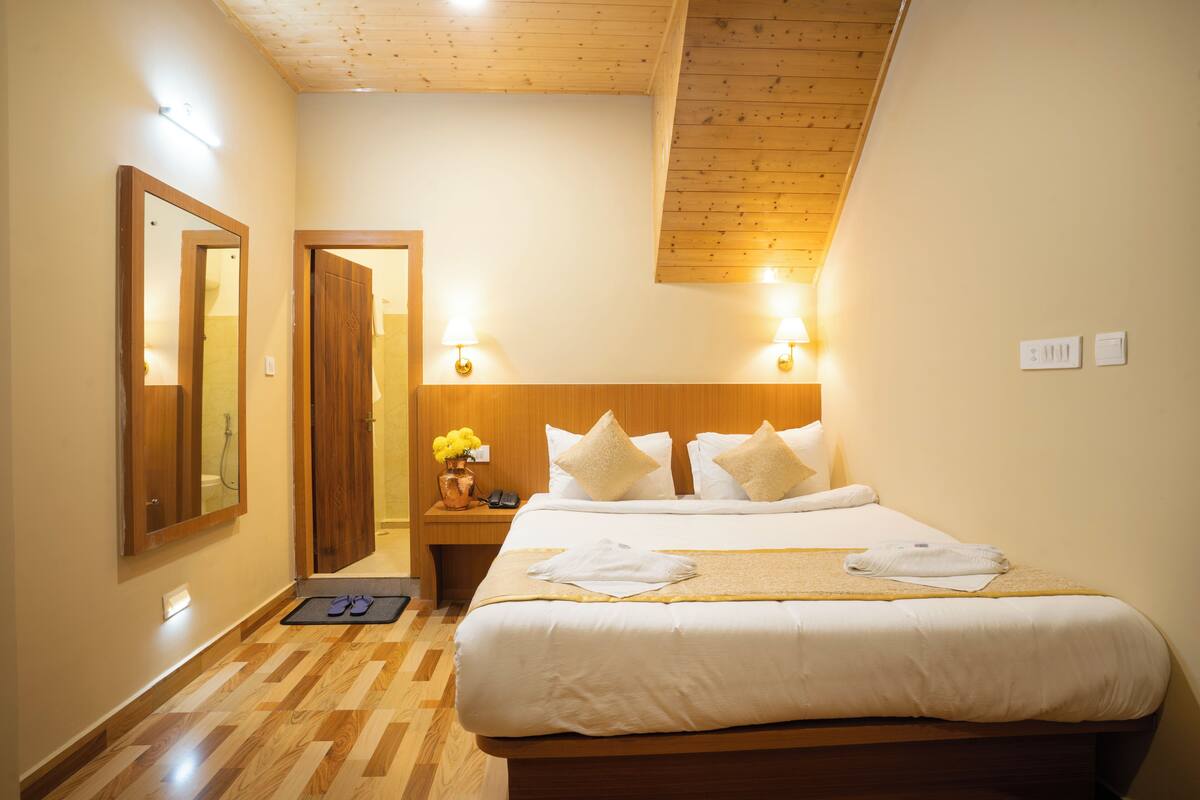 A hotel room with a large bed, wooden headboard, two bedside lamps, a nightstand with a phone, and a wooden floor.