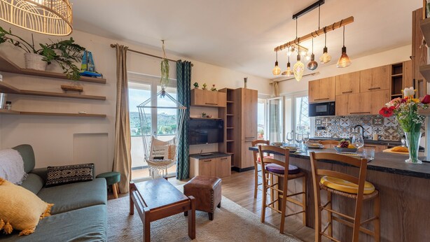 A modern kitchen with wooden cabinets, a dining area with a sofa and table, and a bar with stools. - Bellissimo Appartamento Vicino al Centro (Sestri Levante)