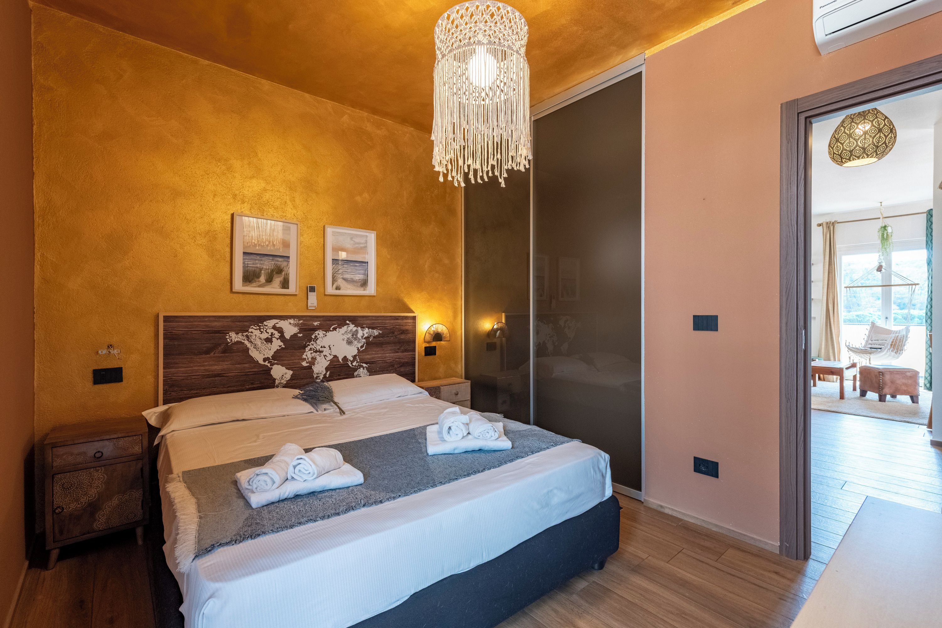 Un dormitorio con una cama, cabecera de madera, un mapa del mundo, dos lámparas fijadas a la pared y una lámpara colgante.