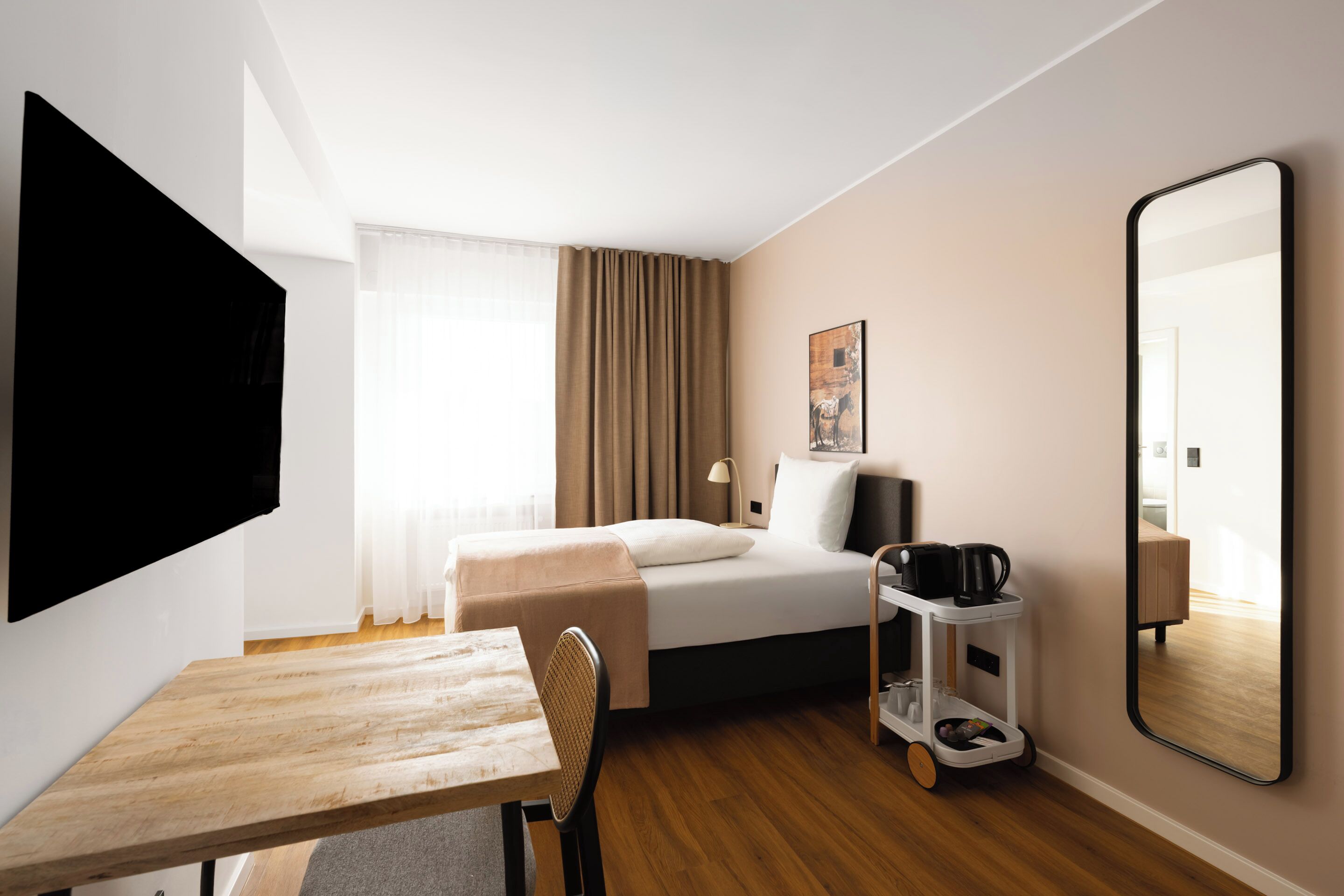A hotel room with a bed, a desk, a chair, a coffee maker, and a mirror.