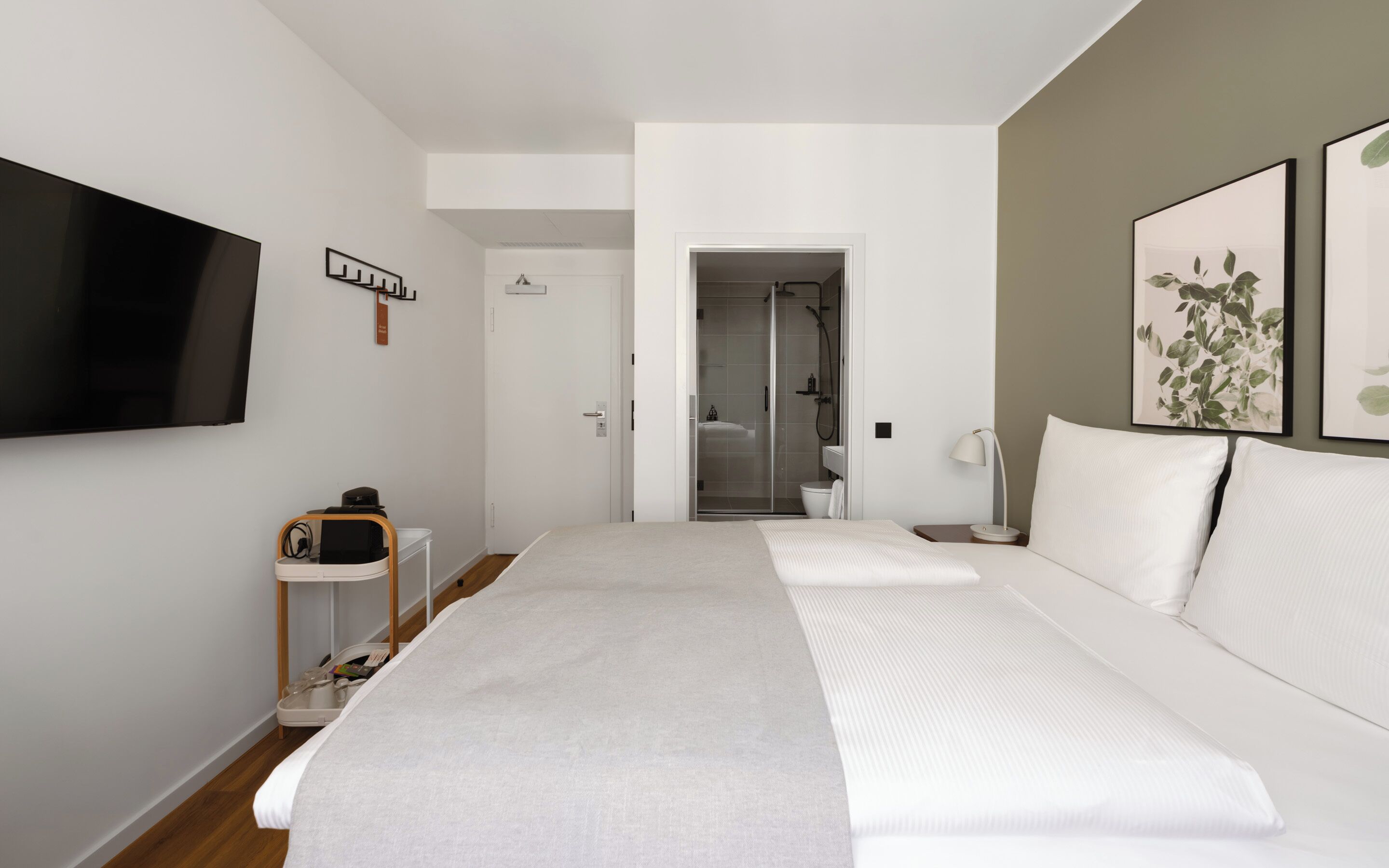Un dormitorio moderno con una cama grande, televisor montado en la pared, zona de ducha y una mesita de noche.