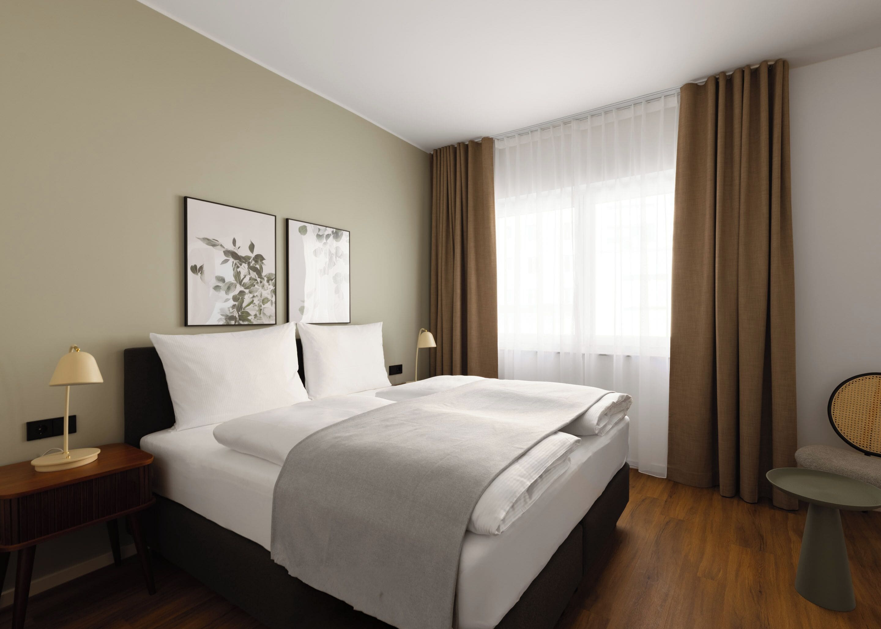 A hotel room with a bed, bedside tables, a chair, and artwork on the wall.