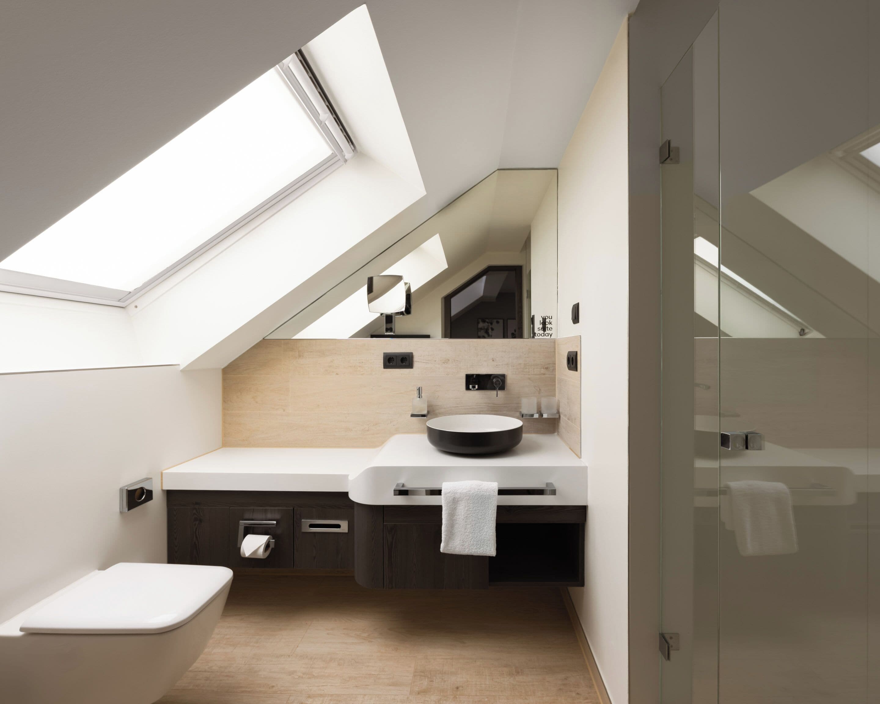 A modern bathroom with a skylight, a freestanding bathtub, a round sink, and a glass shower enclosure.
