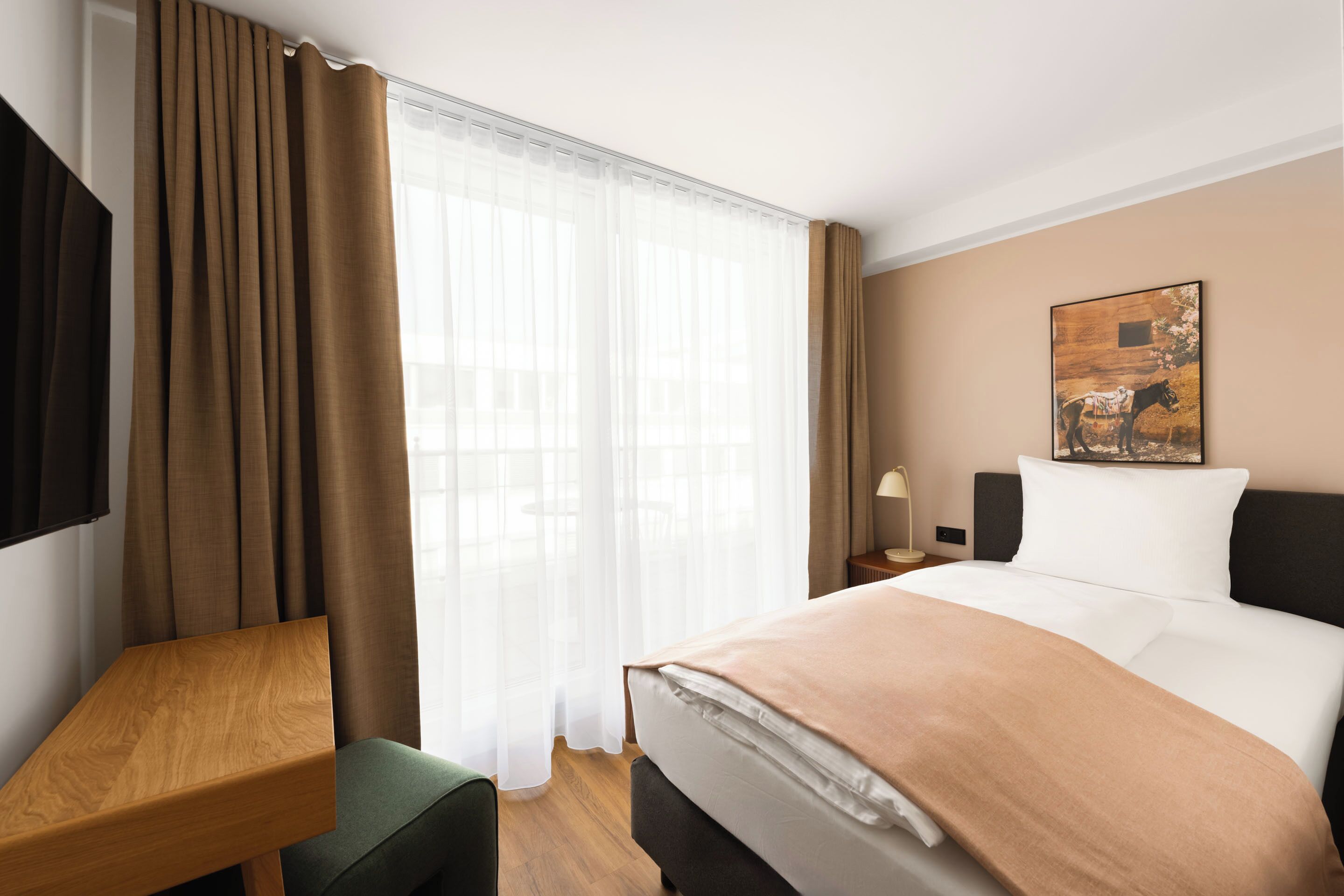 A hotel room with a bed, a desk, a chair, a TV, a painting on the wall, and a window with curtains.