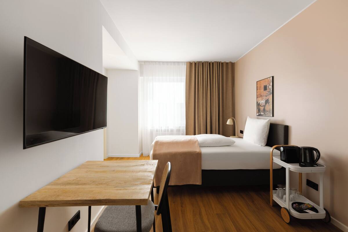 Ein Hotelzimmer mit einem Bett, einem Fernseher, einem Tisch und einem Wagen mit einer Kaffeemaschine.