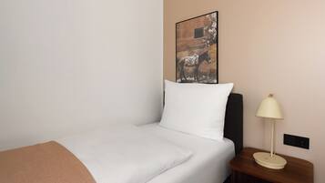 Een keurig opgemaakt bed met een wit kussen en een bruine deken, een nachtkastje met een lamp, en een aan de muur hangend schilderij van een paard.