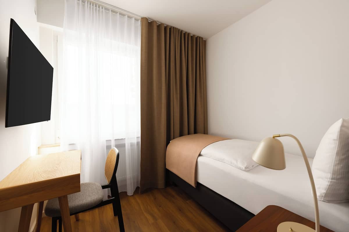 Ein Hotelzimmer mit Bett, Schreibtisch, Stuhl, Fernseher und Lampe.