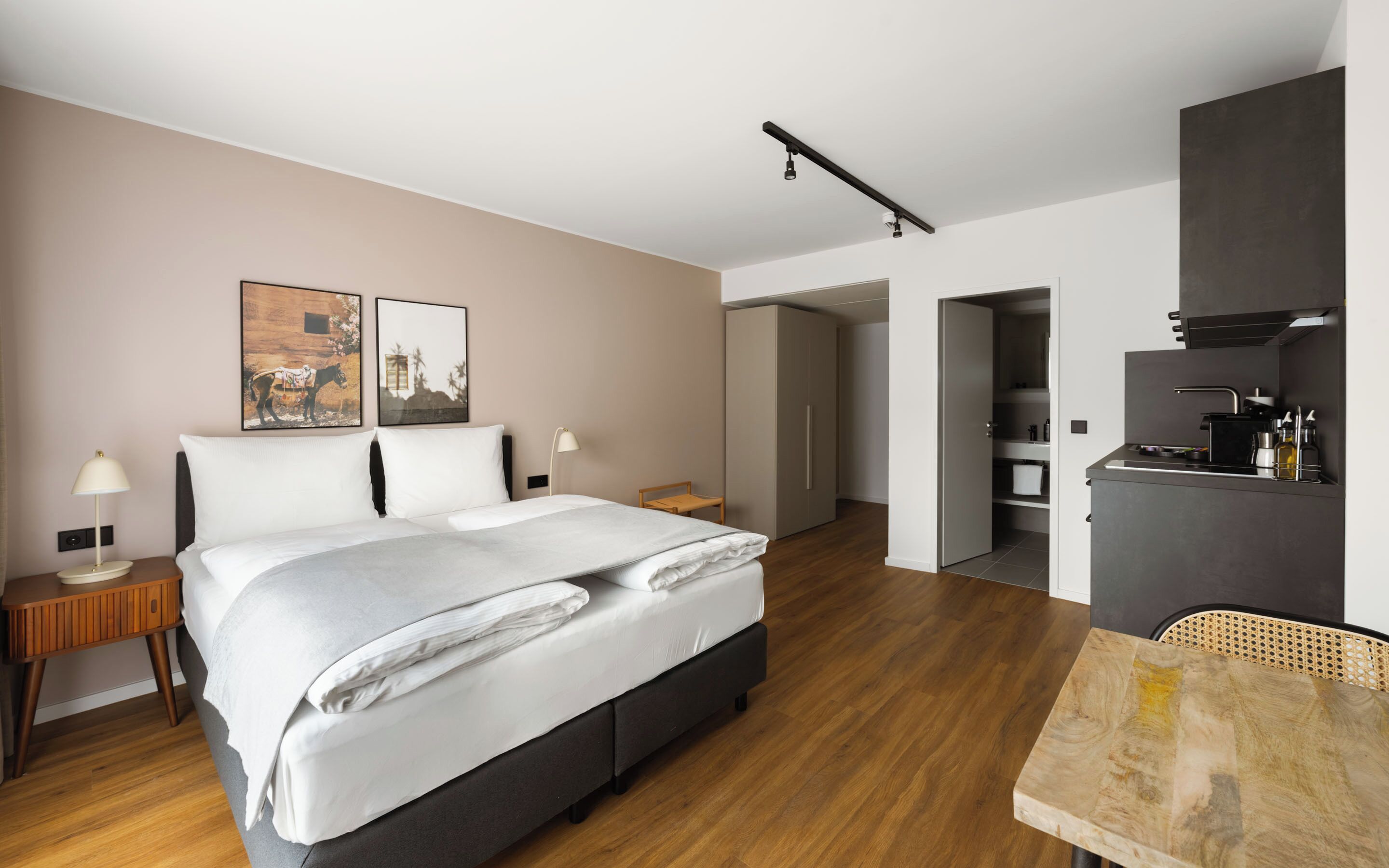 Una habitación de hotel moderna con cama, mesitas de noche, escritorio, silla, armario y kitchenette.