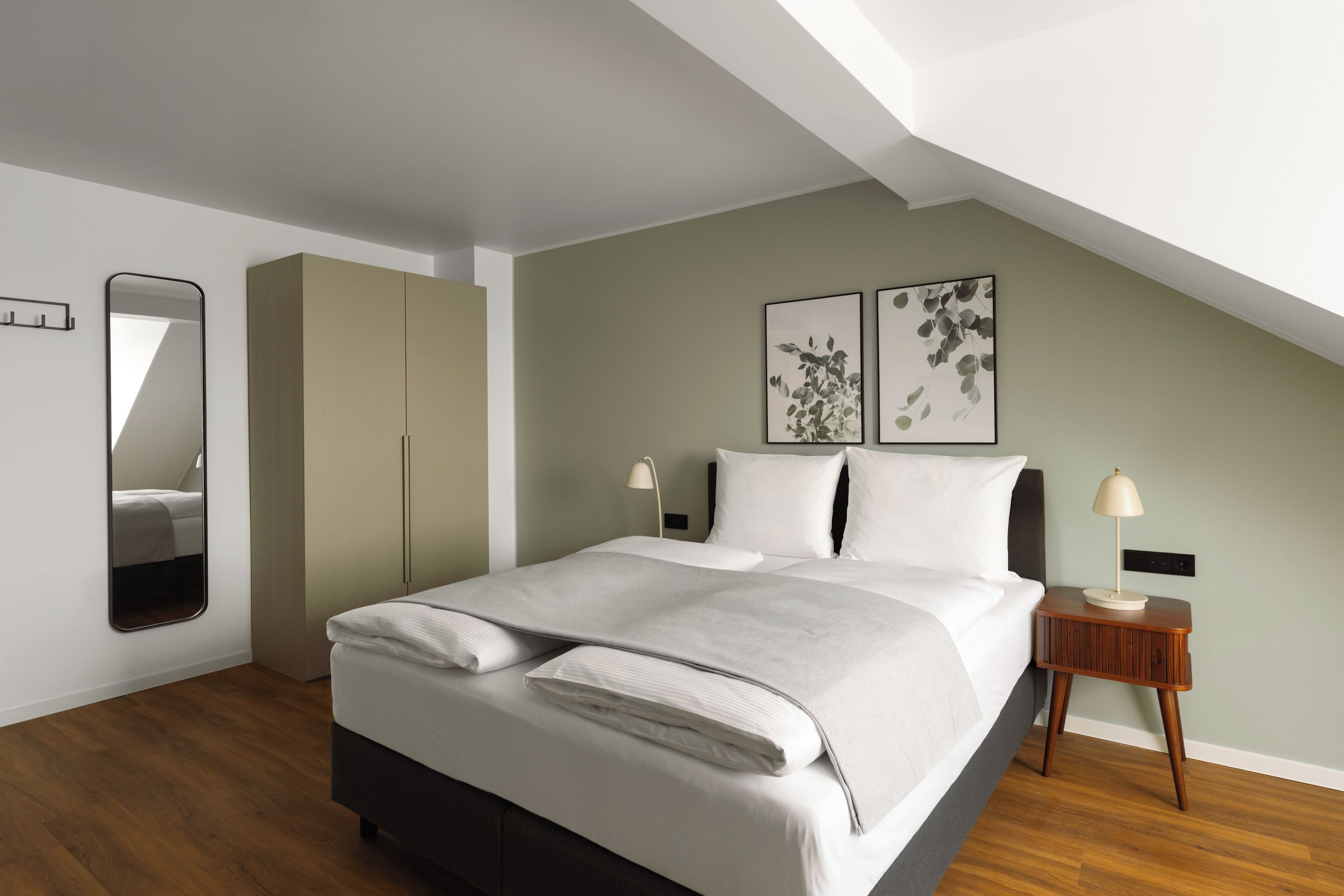 A bedroom with a bed, a wardrobe, a nightstand, and two wall-mounted artworks.