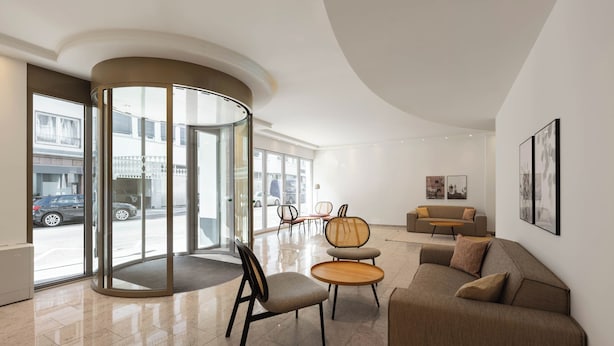 A modern lobby with a curved glass wall, a roundabout seating area, a sofa, and a coffee table. - Limehome Düsseldorf Kö (Düsseldorf)