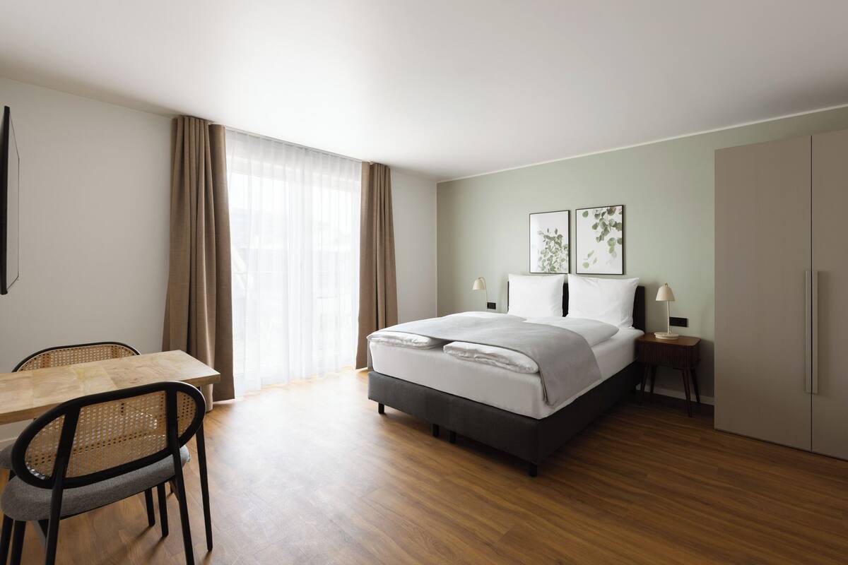 Ein modernes Hotelzimmer mit Bett, Nachttischen, Schreibtisch und Kleiderschrank.
