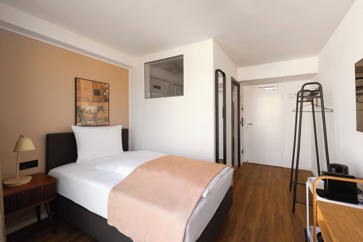 Ein Hotelzimmer mit Bett, Nachttisch, Lampe und einem Gemälde an der Wand.