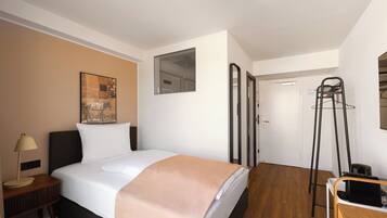 A hotel room with a bed, bedside table, lamp, and a painting on the wall.