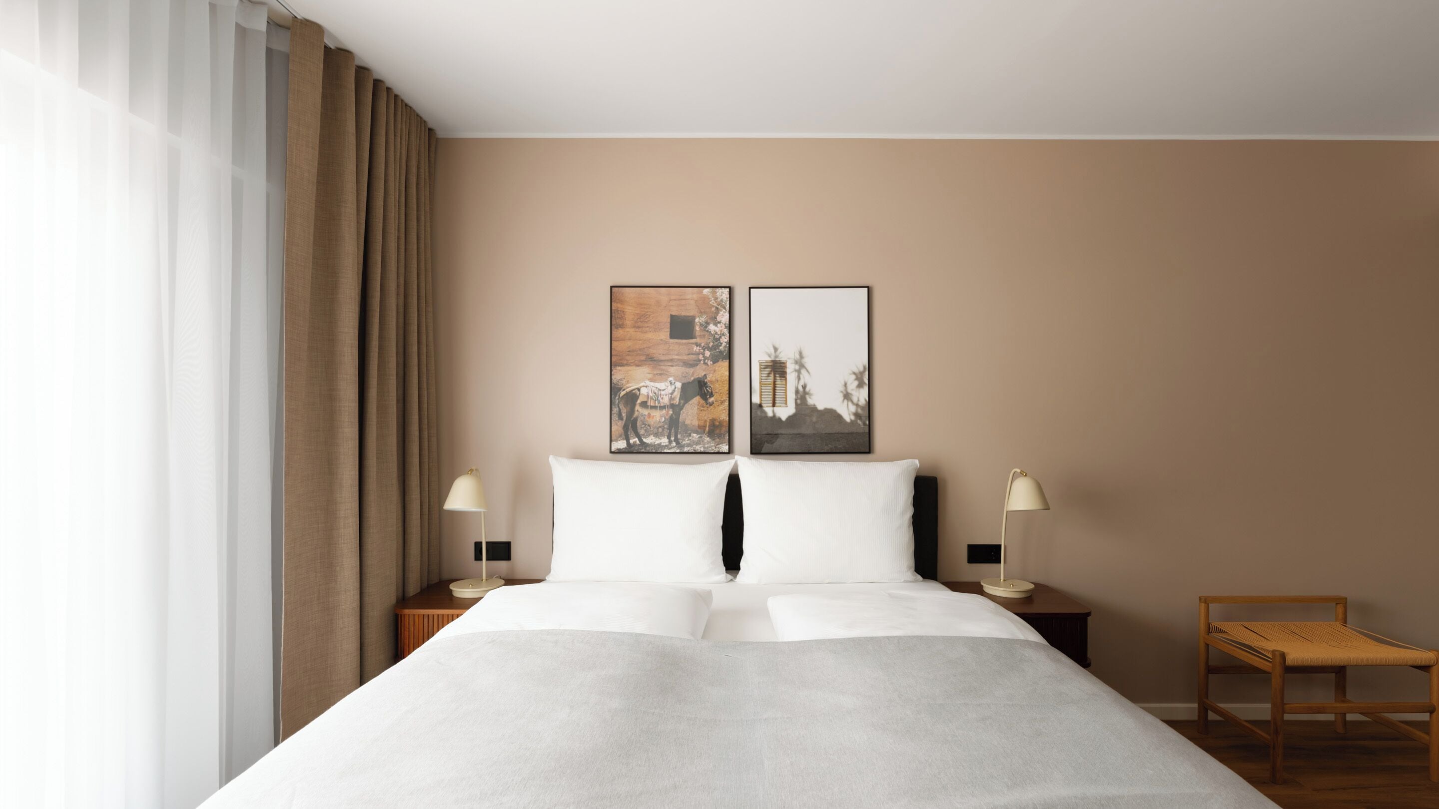 A hotel room with a large bed, two bedside tables with lamps, a wooden chair, and two framed pictures on the wall.