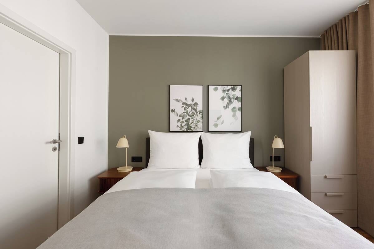 Ein Hotelzimmer mit einem großen Bett, zwei Nachttischen mit Lampen, einem Kleiderschrank und zwei Wandbildern.