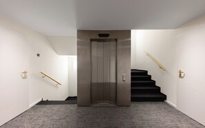 Een modern interieur met een metalen lift, een trap met een zwart tapijt en een wandlamp.