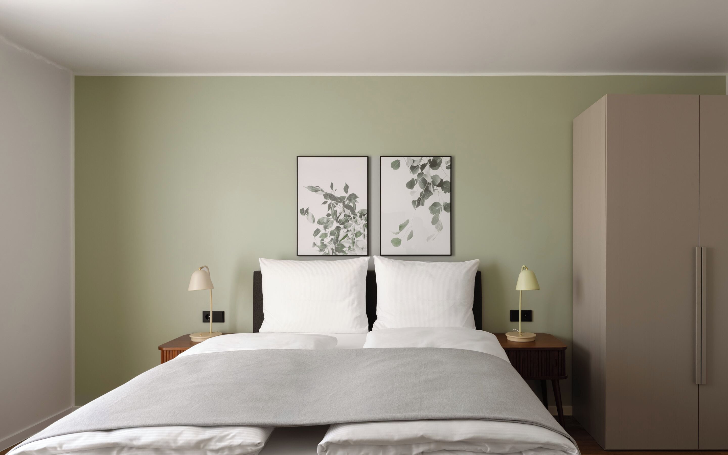 A neatly made bed with white linens, two bedside tables with lamps, and two framed wall art pieces above the bed.