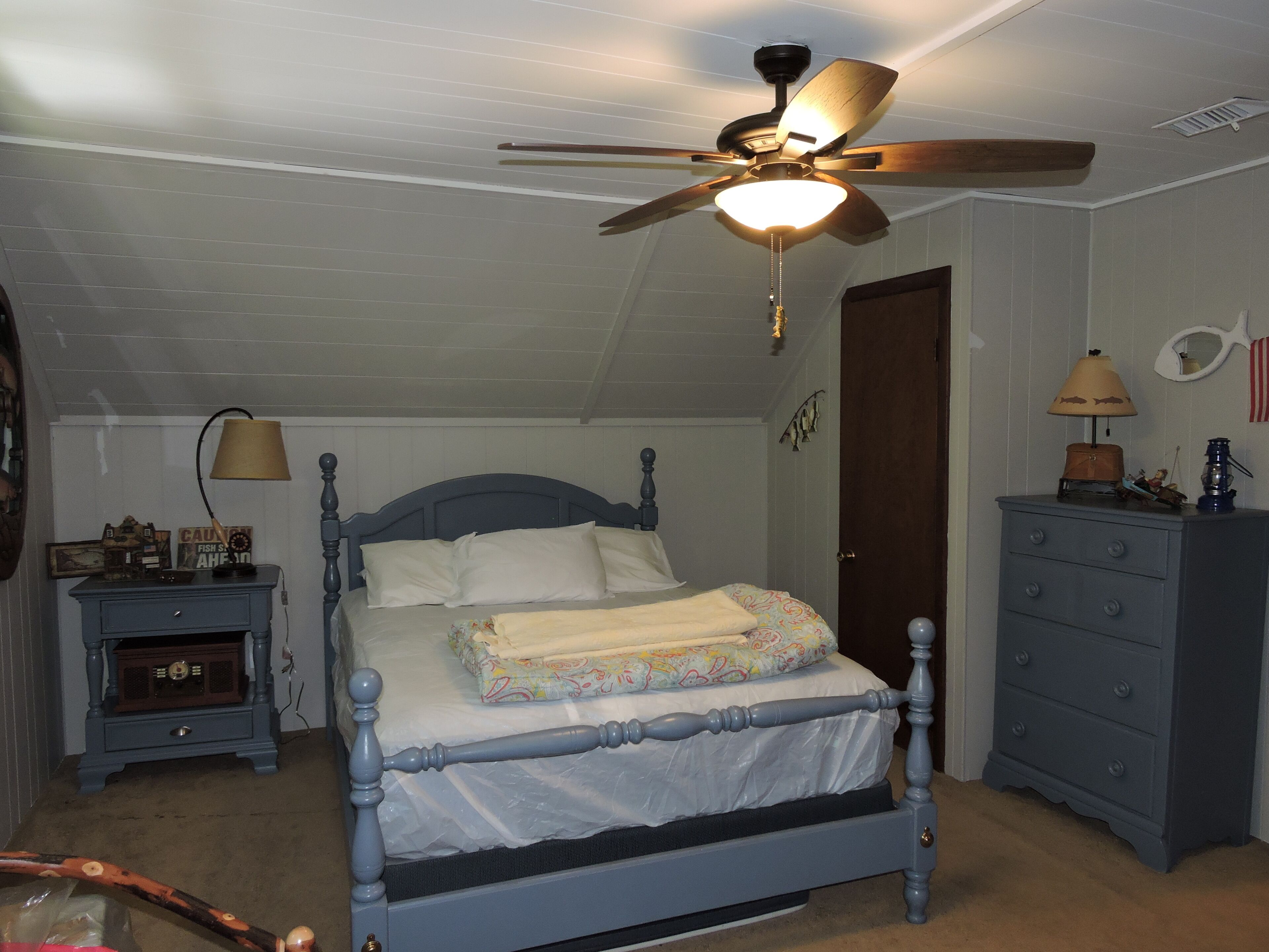 Une chambre à coucher comprenant un lit, un ventilateur de plafond, une commode, une table de chevet et une lampe.