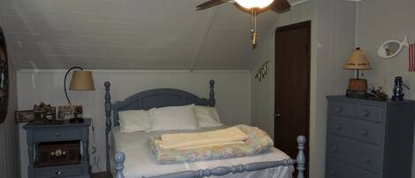 Une chambre à coucher comprenant un lit, un ventilateur de plafond, une commode, une table de chevet et une lampe.