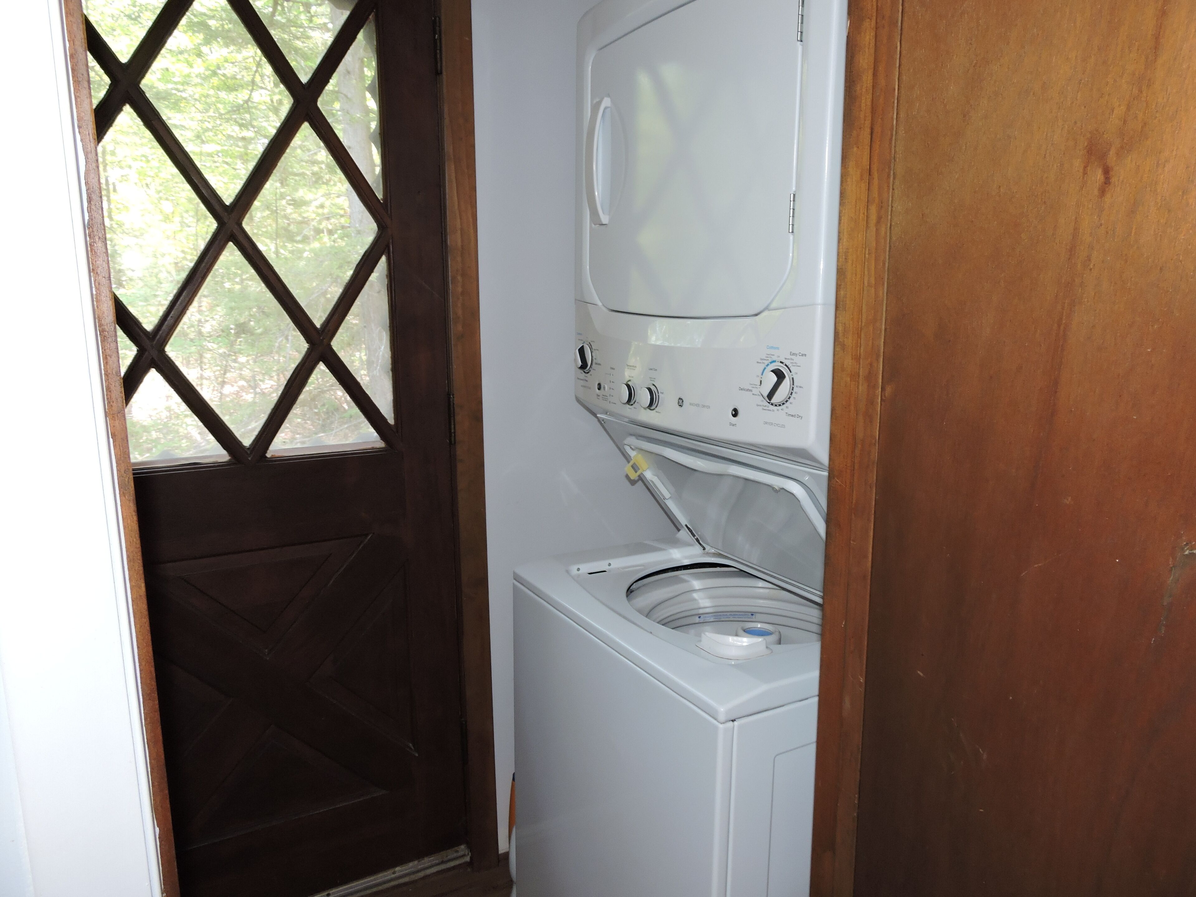 A laundry room with a washer and dryer, wooden door, and a window with a lattice design.