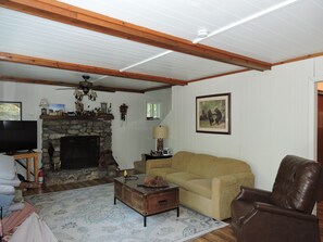Ein Wohnzimmer mit Kamin aus Stein, einem Fernseher, einer Couch, einem Couchtisch und einem braunen Ledersessel.