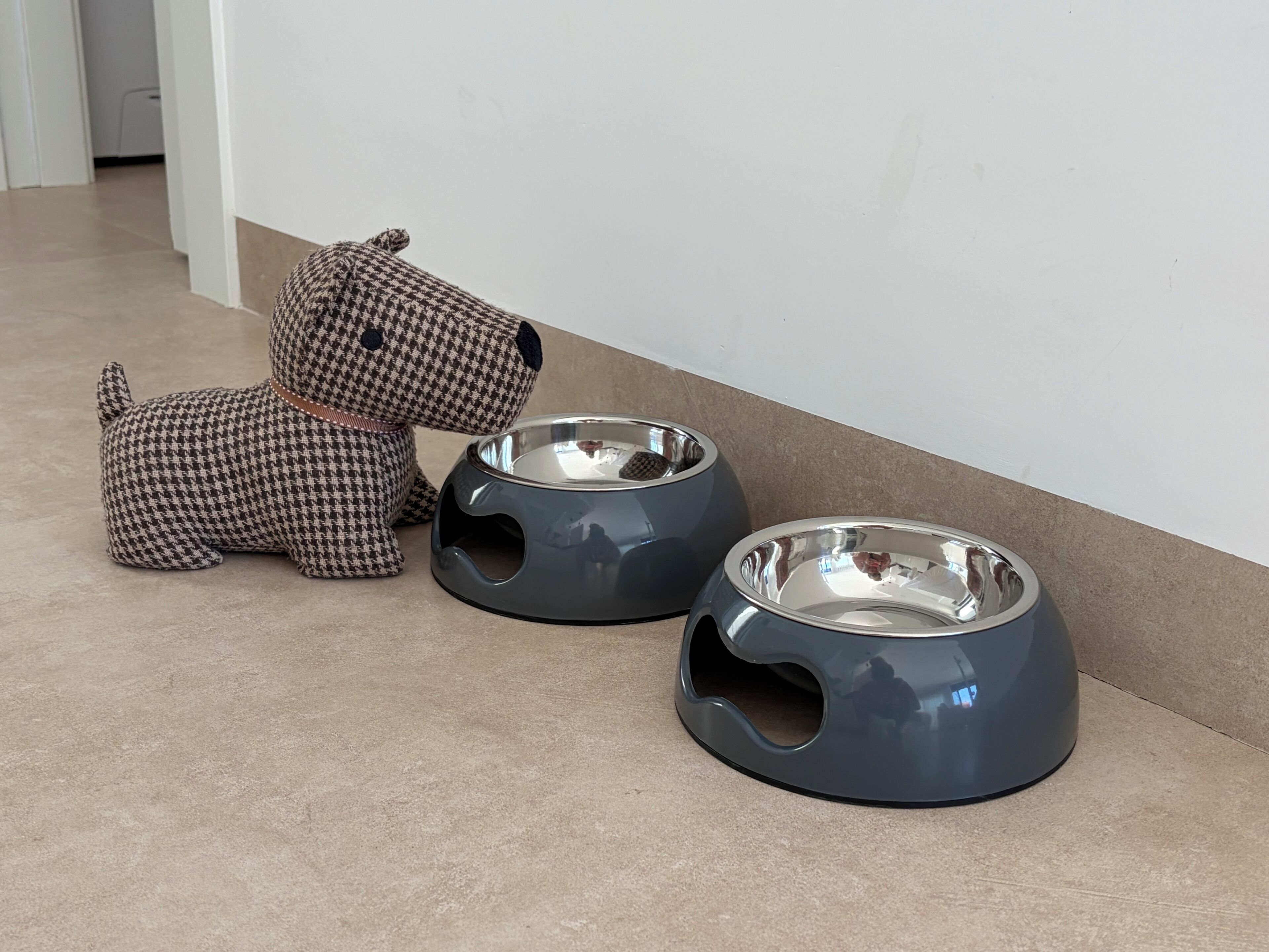 Een hondenspeeltje met een streepjespatroon en twee metalen hondenkommen op een betegelde vloer.