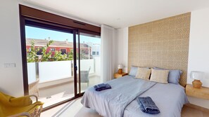 A bedroom with a bed, a nightstand, a lamp, a chair, and a view of buildings outside.