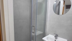 Une salle de bain dotée d’une douche à parois de verre, d’un lavabo blanc avec un plan de toilette en marbre et d’un miroir rond fixé au mur.