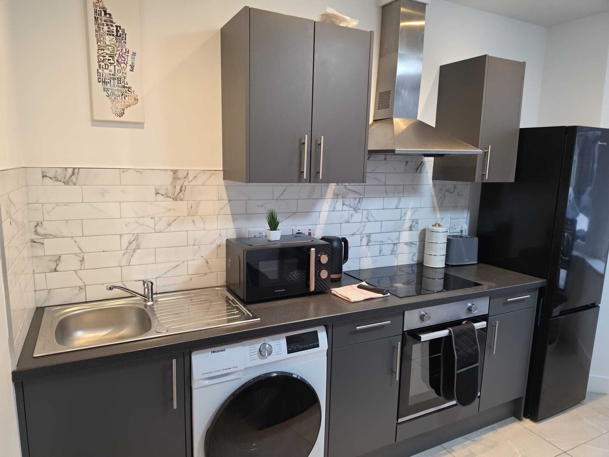 A modern kitchen with grey cabinets, a stainless steel sink, a microwave, a toaster, a kettle, and a washing machine.