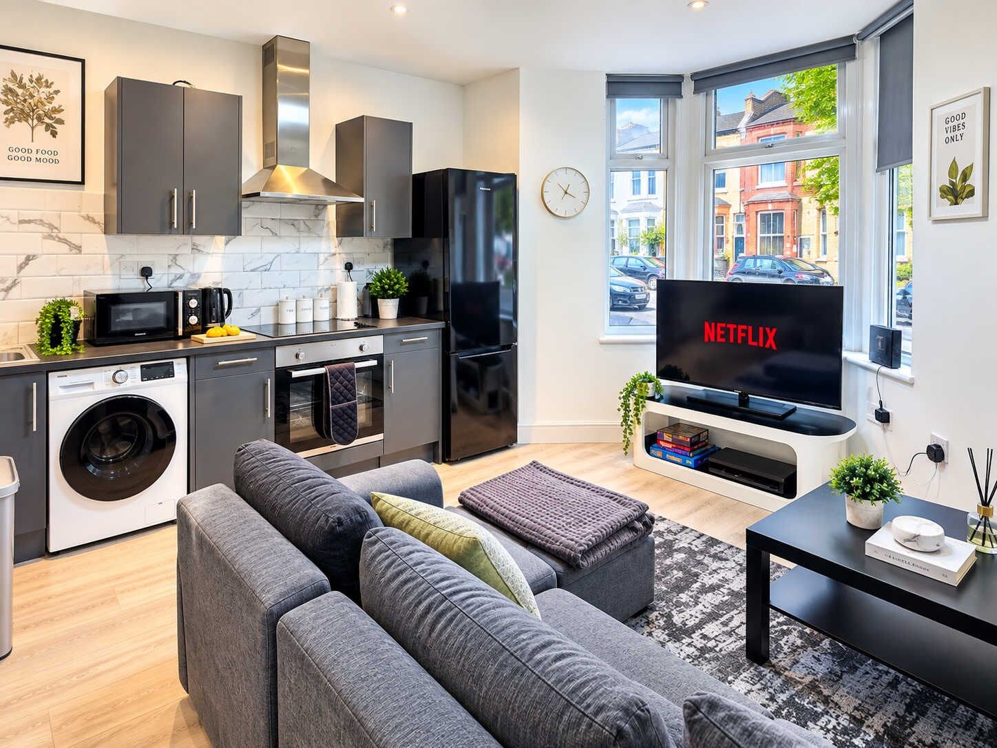 A modern kitchen with a washing machine, microwave, and a large black refrigerator.