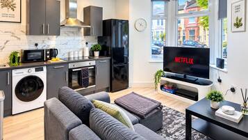 A modern kitchen with a washing machine, microwave, and a large black refrigerator.
