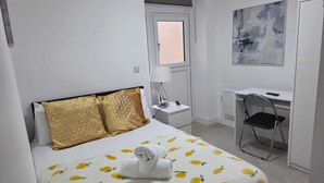 Habitación de hotel con cama, escritorio, silla, lámpara y un cuadro en la pared.