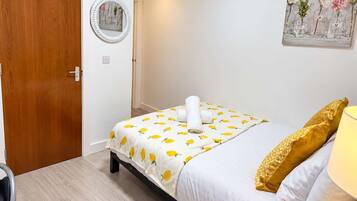 A bedroom with a bed, a bedside table, a lamp, a door, and a wall decoration.