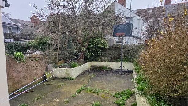 Un jardin arrière d’une maison, comprenant un panier de basketball, un mur en pierre et un espace aménagé en jardin.