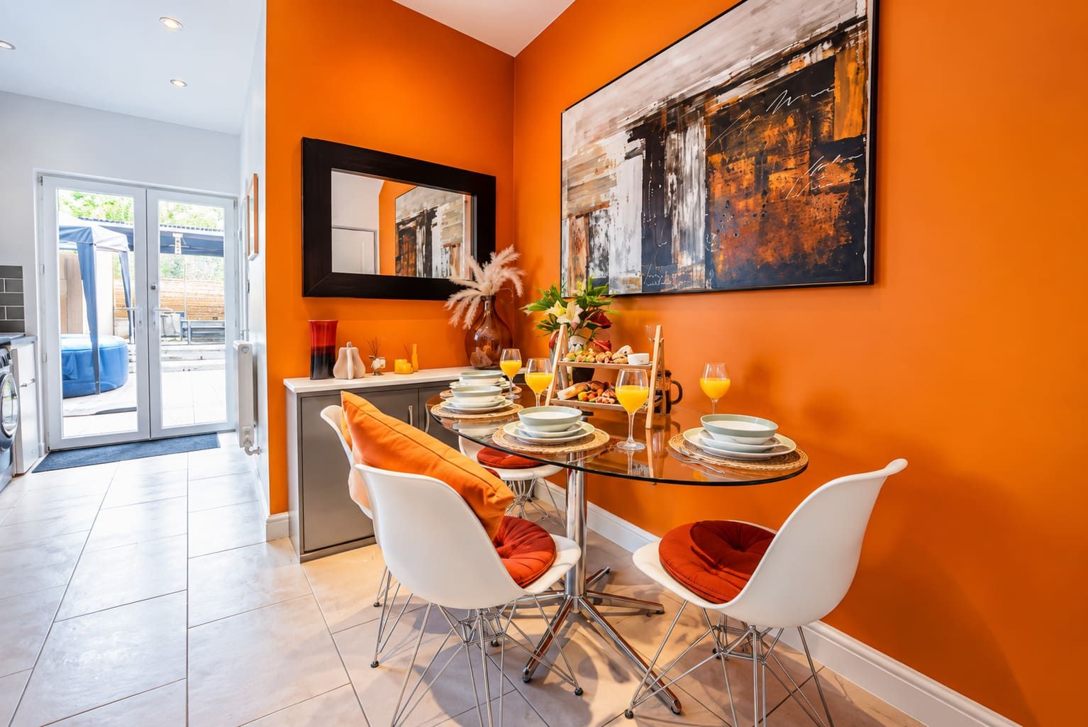 A dining area with a glass table, white chairs, and orange cushions.